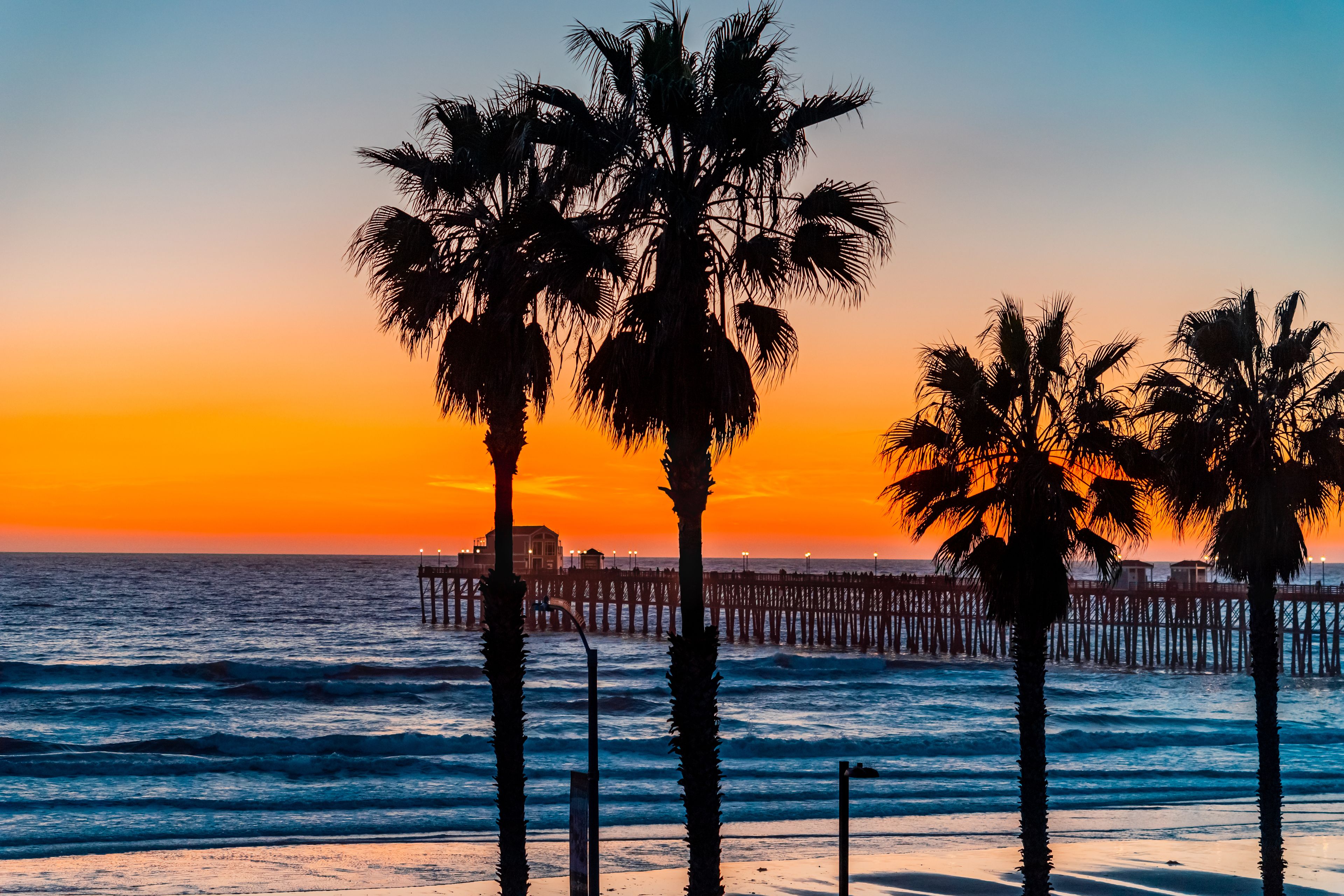 A sunset over the ocean with palm trees and a pier.