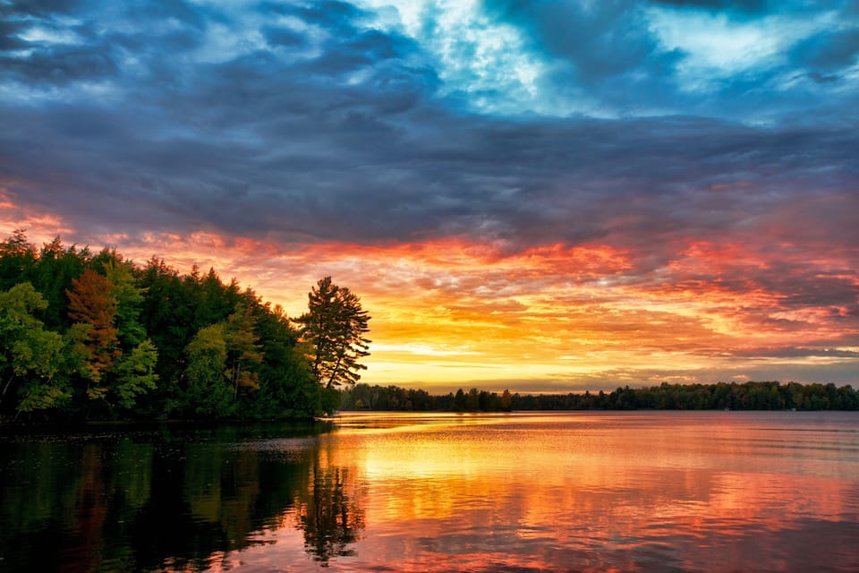 Un coucher de soleil sur un lac, avec une rive bordée d’une forêt.