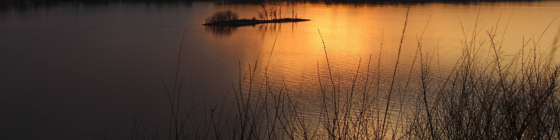 A sunset over a calm lake with a small island in the center.