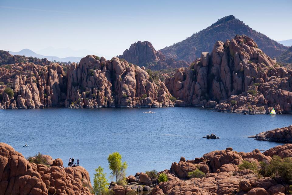 Paisagem rochosa com uma grande massa de água, montanhas ao fundo e um pequeno barco na água.