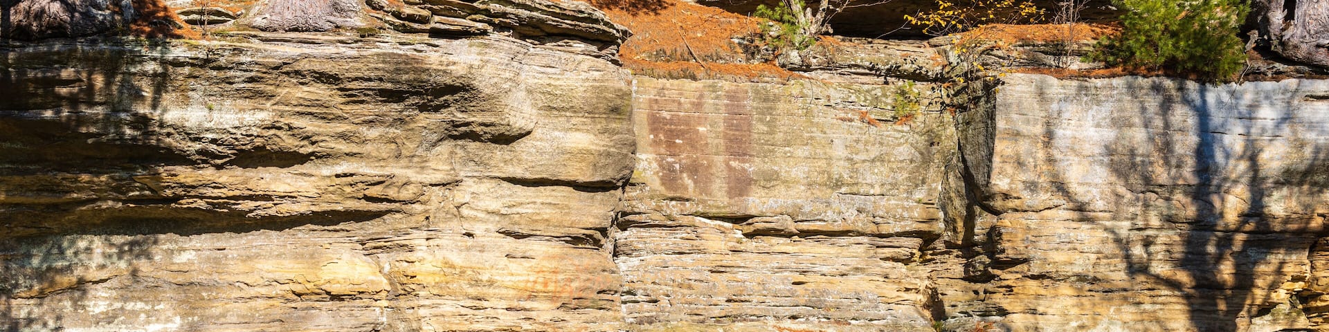 Un puente de piedra con barandilla roja que conduce a la entrada de una cueva en un acantilado rocoso.