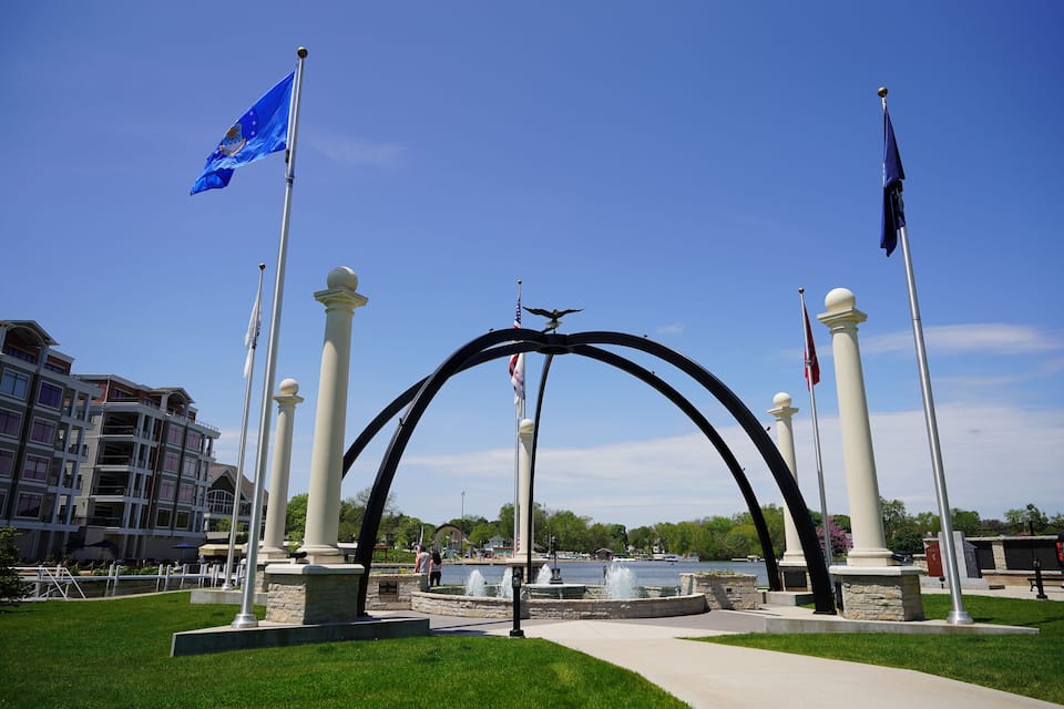 A park with a fountain, flags, and a building in the background.