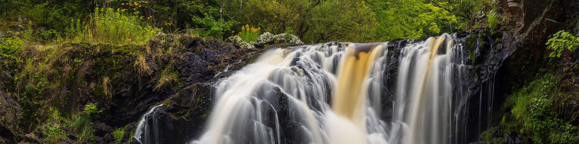 Una cascada se precipita sobre rocas hacia un río rodeado de exuberante vegetación.