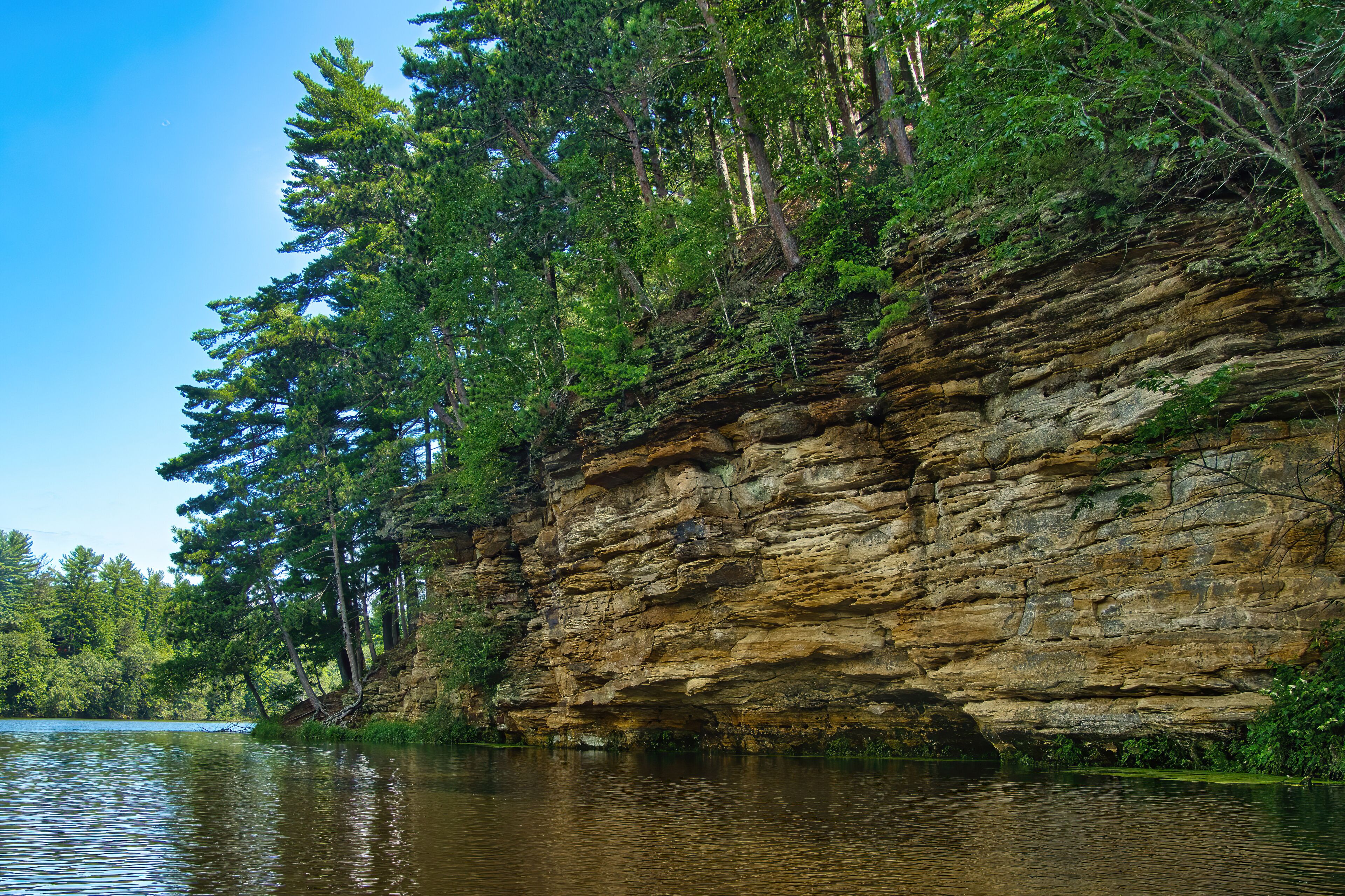 Summer’s day closeup of sandstone cliffs and a lush green forest along the banks of Mirror Lake, near Baraboo, Wisconsin.