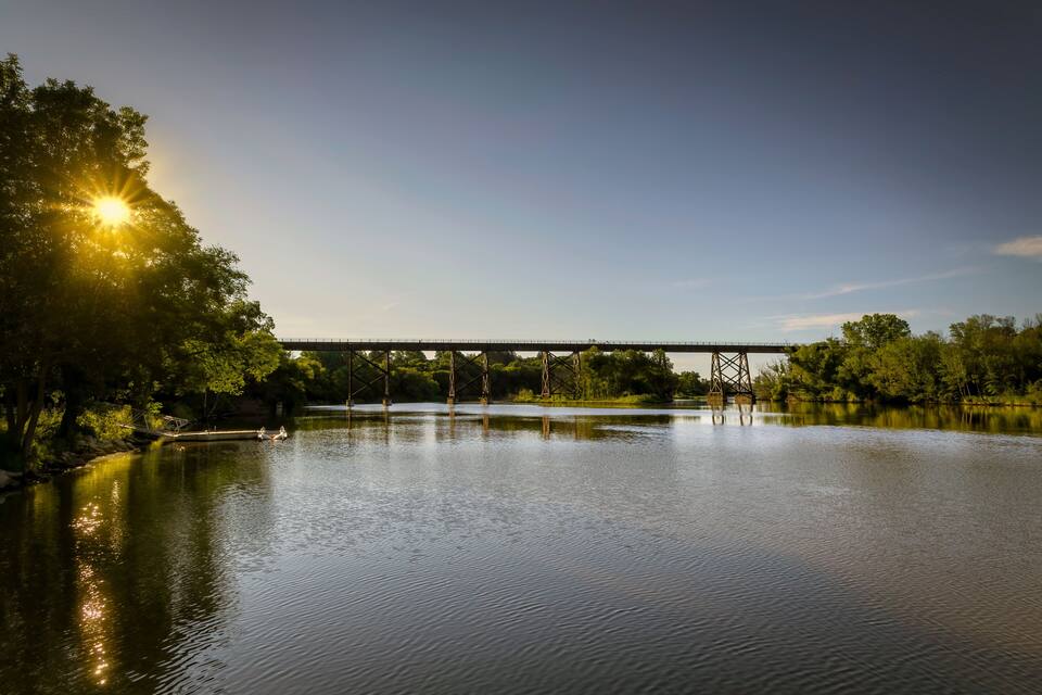 A calm river with a bridge and trees reflecting the sunlight.