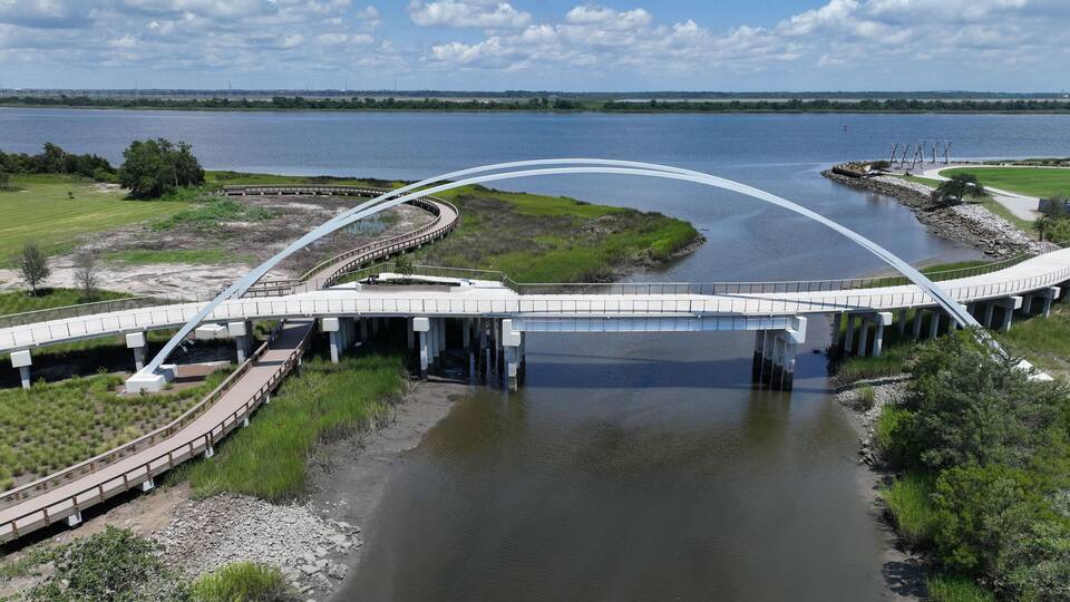 A large, arched bridge over a river with grassy banks and a distant city skyline.