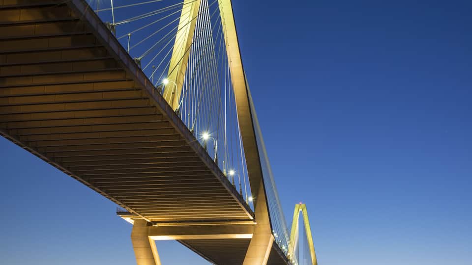 A cable-stayed bridge at dusk with illuminated cables and a clear sky.