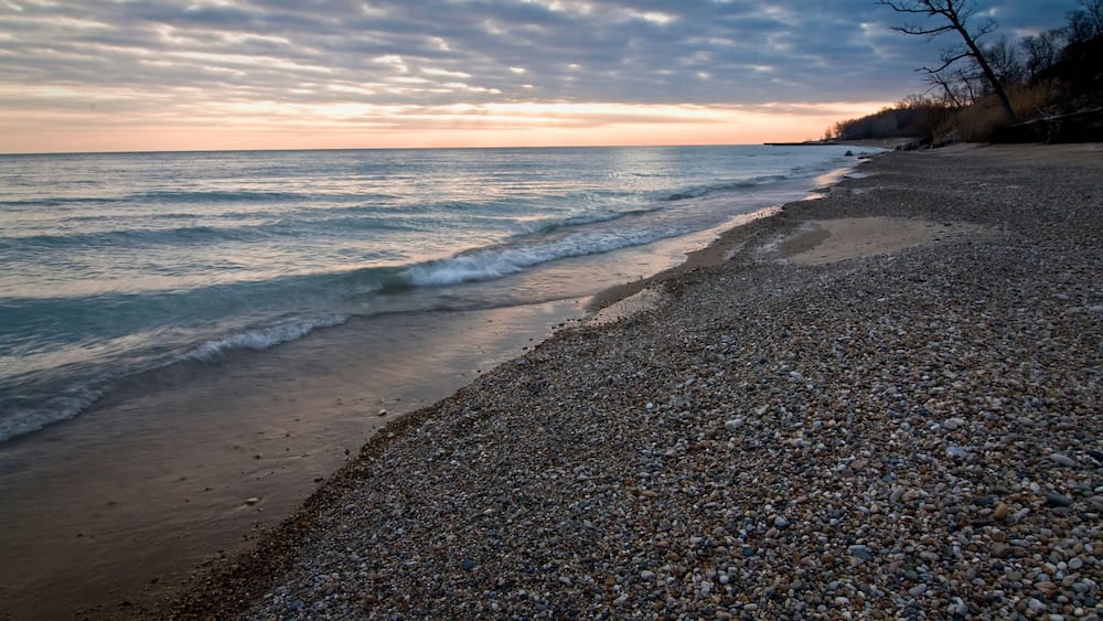 Ein Kiesstrand mit Wellen im Abendlicht.