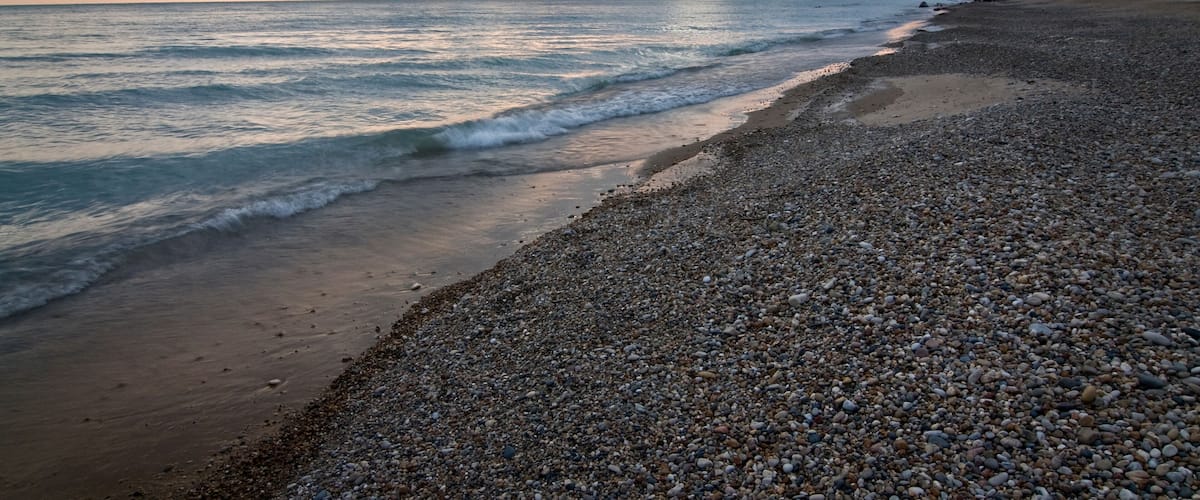 A pebbly beach with waves at sunset.