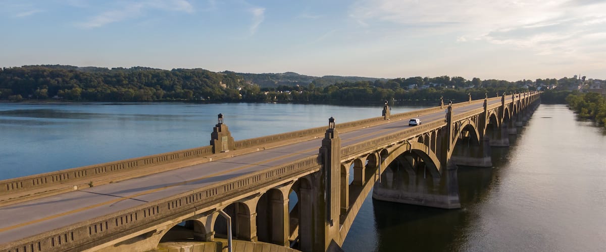 A long bridge spanning a river with multiple arches, surrounded by hills and trees.