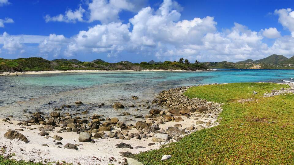 A tropical beach with clear turquoise waters, rocky shorelines, and lush greenery.