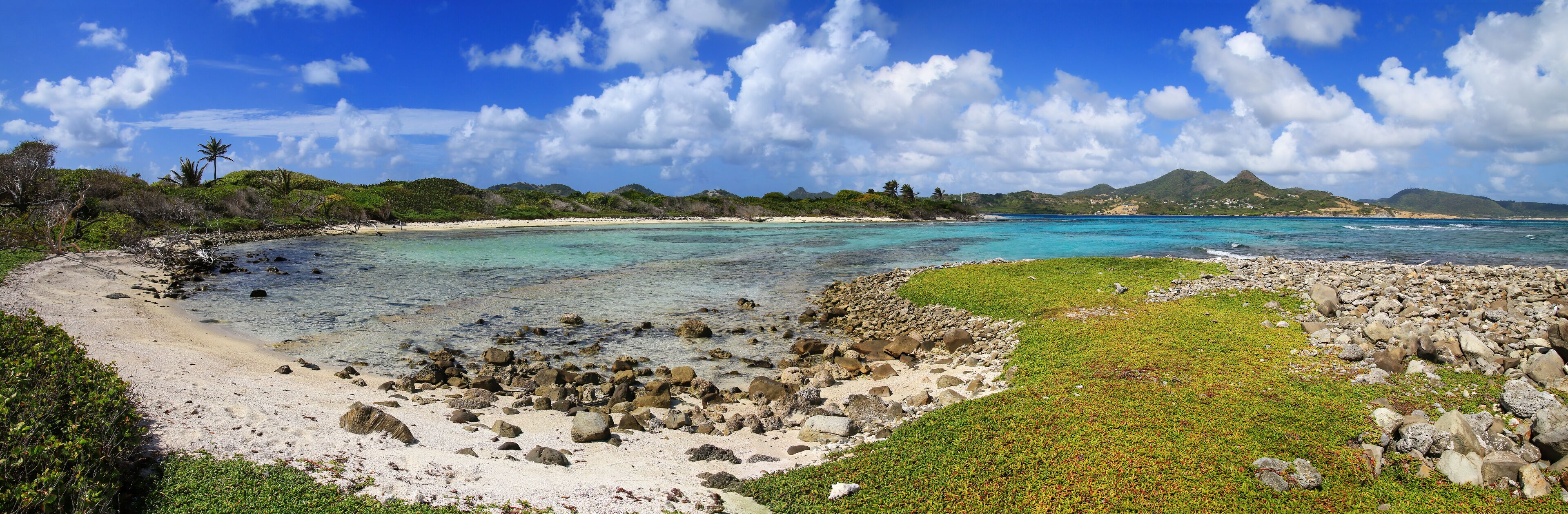 A tropical beach with clear turquoise waters, rocky shorelines, and lush greenery.