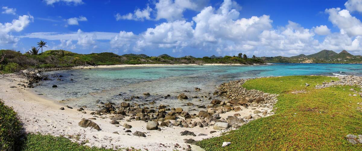 A tropical beach with clear turquoise waters, rocky shorelines, and lush greenery.