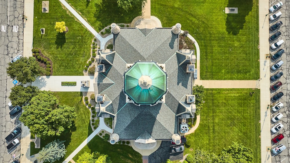 An aerial view of a park with a central gazebo, surrounding pathways, and parked cars.