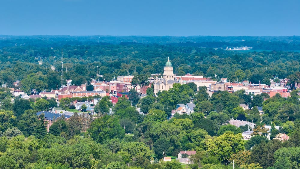 A town with a prominent historic building with a dome, surrounded by dense green trees and residential houses.