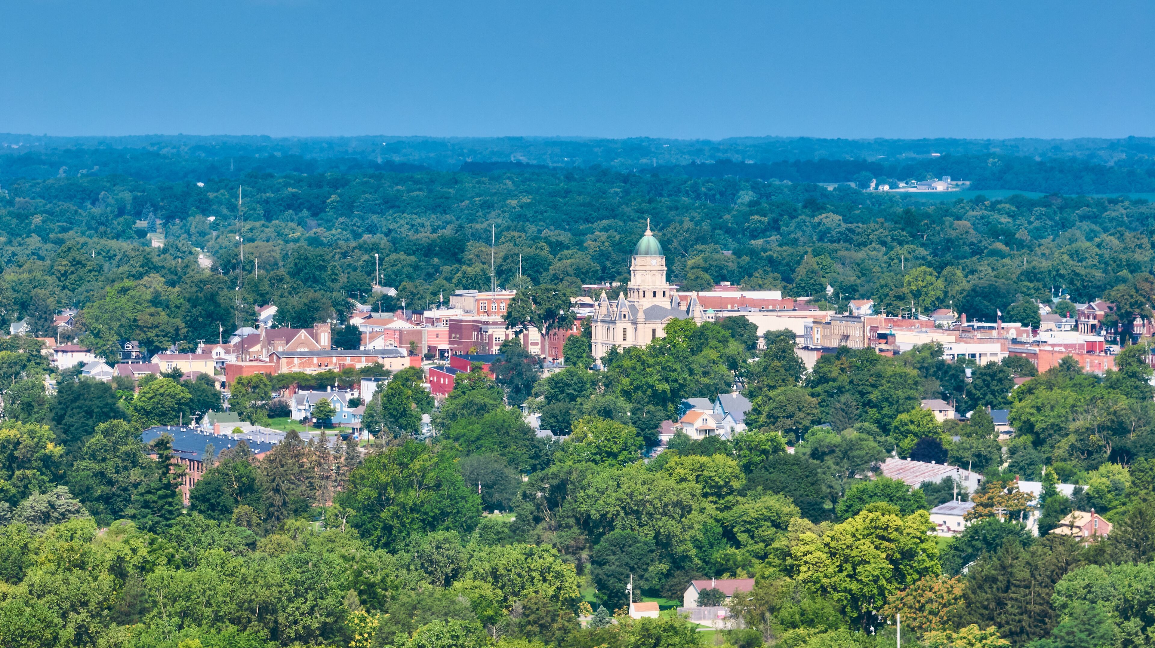A town with a prominent historic building with a dome, surrounded by dense green trees and residential houses.