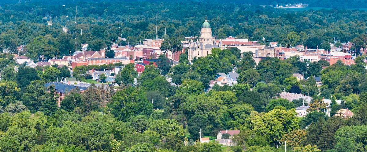 A town with a prominent historic building with a dome, surrounded by dense green trees and residential houses.