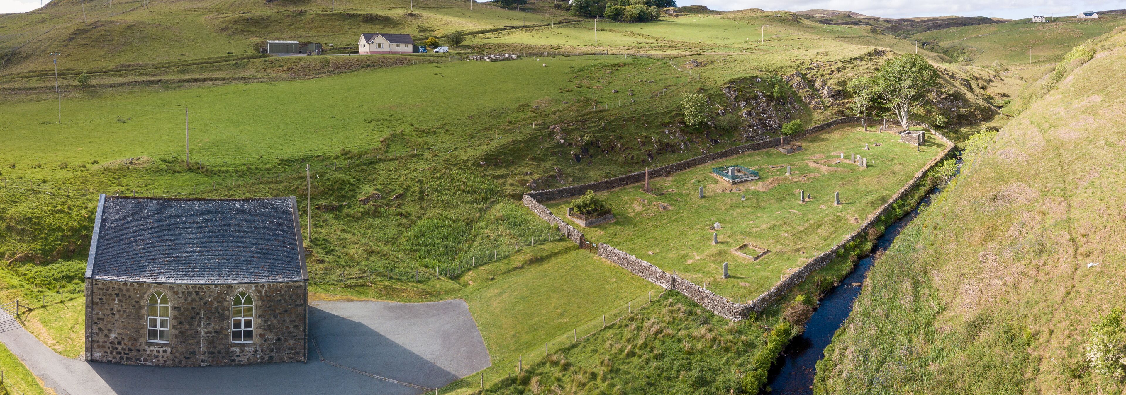 A stone church, a cemetery, and a stone wall in a rural landscape.