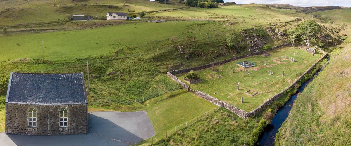 A stone church, a cemetery, and a stone wall in a rural landscape.