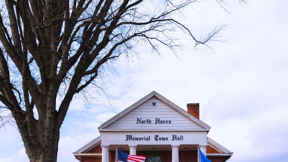 A brick building with a white entrance, labeled 'North Haven Memorial Town Hall,' featuring an American flag and a wreath.