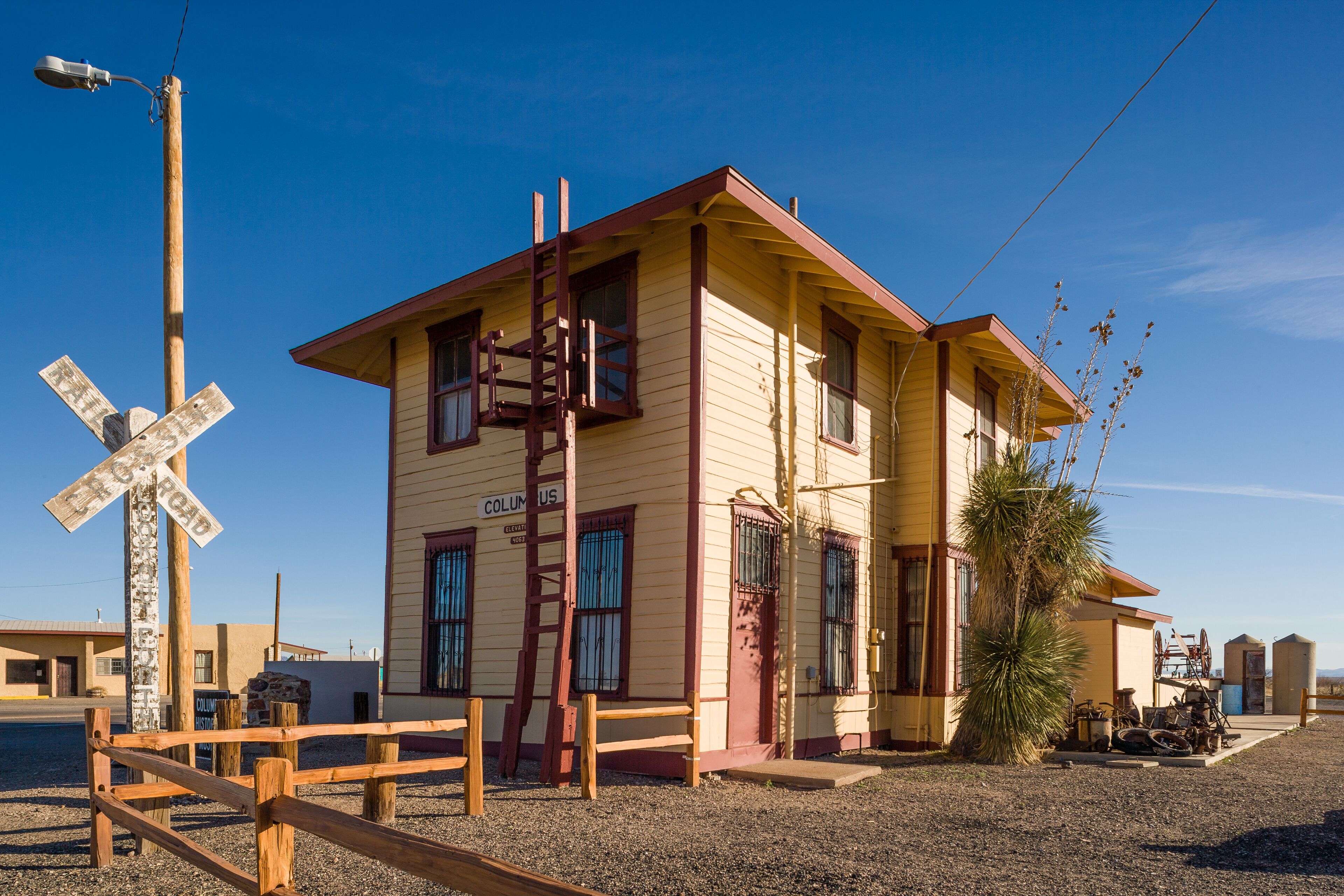 A yellow building with a red roof, a wooden fence, and a railroad crossing sign.