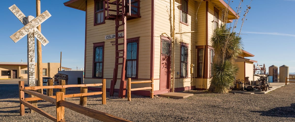 A yellow building with a red roof, a wooden fence, and a railroad crossing sign.