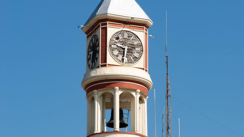 A clock tower with Roman numerals and a red roof.