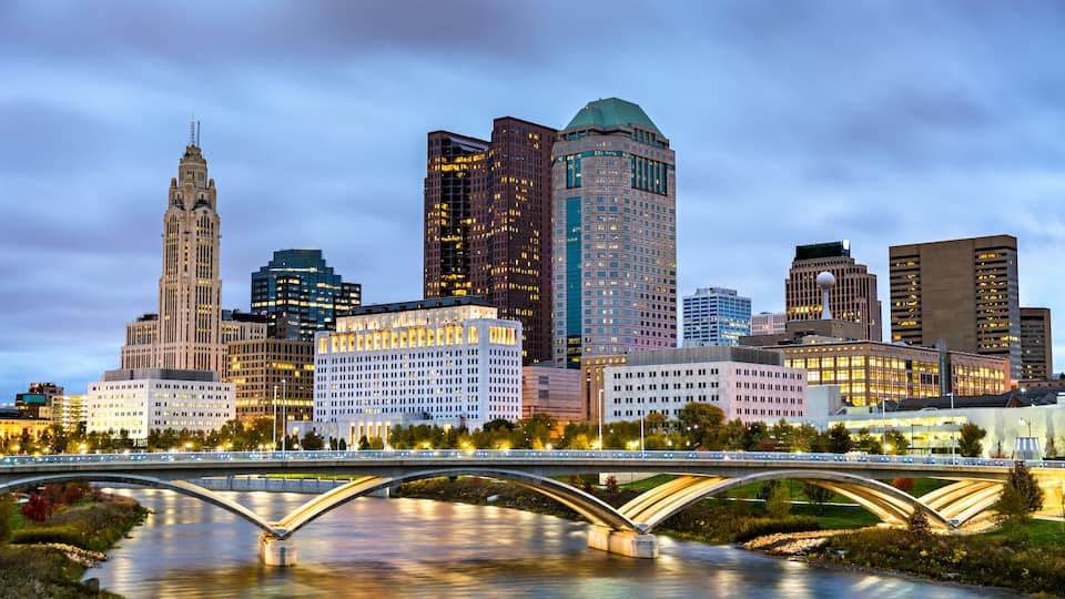 A city skyline with a prominent historic building, a modern skyscraper, and a river with a bridge.