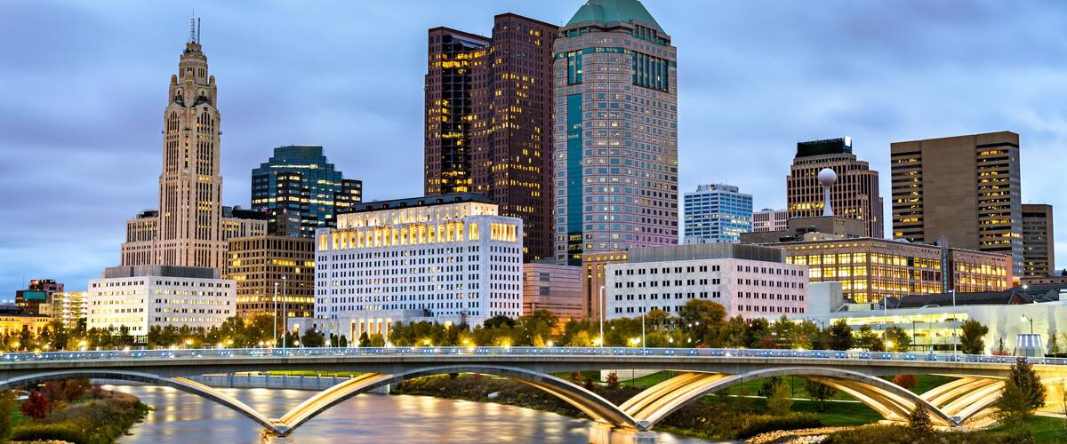 A city skyline with a prominent historic building, a modern skyscraper, and a river with a bridge.