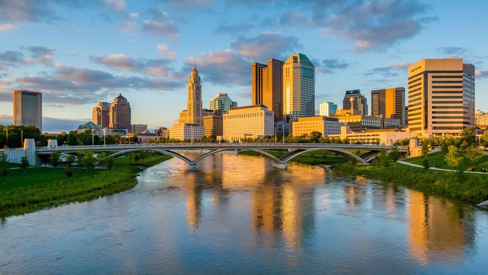 A city skyline with modern buildings, a river, and a bridge.