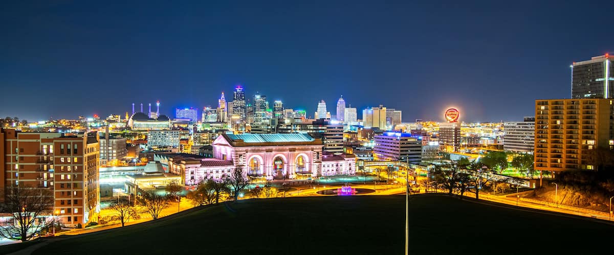 A city skyline at night with illuminated buildings and a prominent pink-lit building in the foreground.