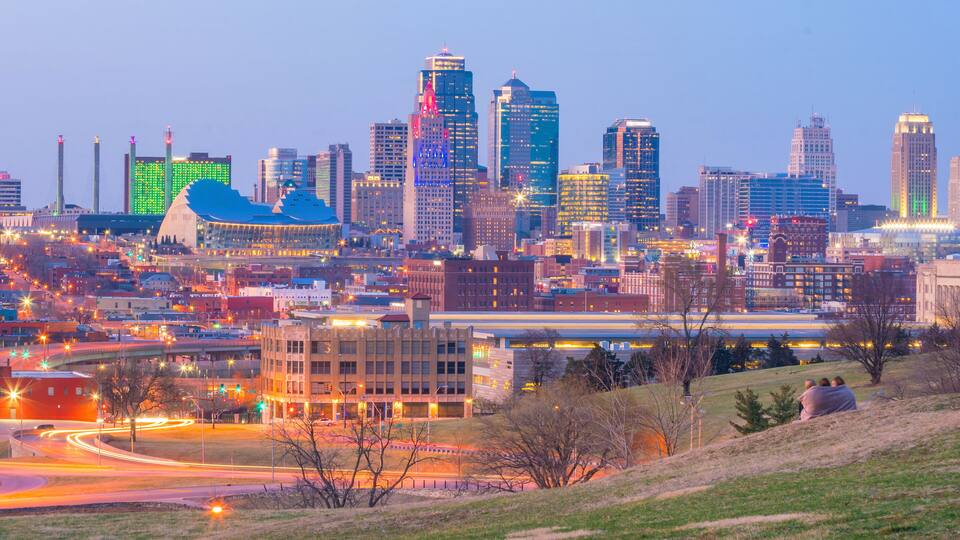A city skyline with illuminated buildings, a large stadium, and a highway with light trails.