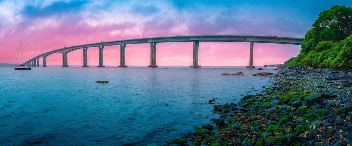 A bridge over water with a boat and rocky shore.