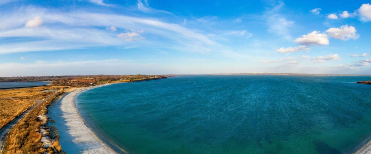A coastal landscape with a clear blue sea, sandy beach, and a road curving along the shore.