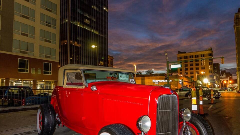 Un coche rojo antiguo estacionado en una calle de la ciudad al anochecer.