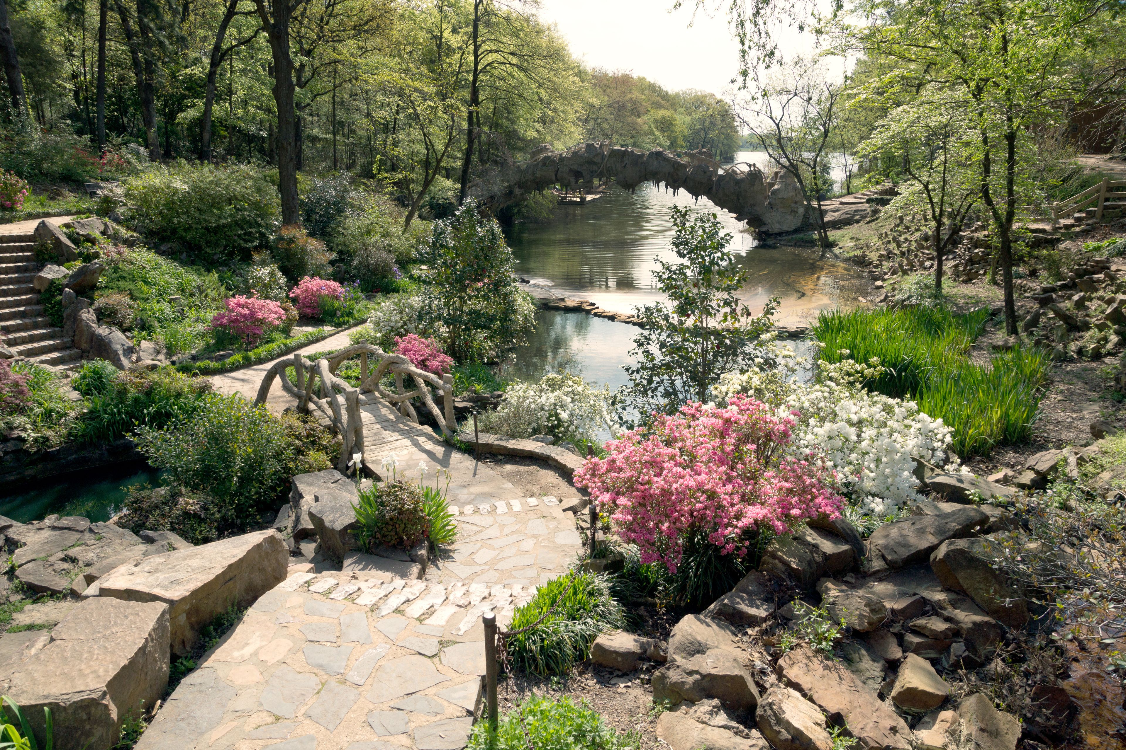 Un puente de piedra sobre un estanque, rodeado de exuberante follaje y plantas en flor.