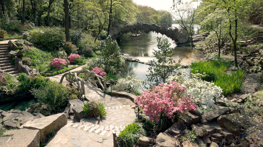 Uma ponte de pedra sobre um lago, rodeada por vegetação exuberante e plantas floridas.