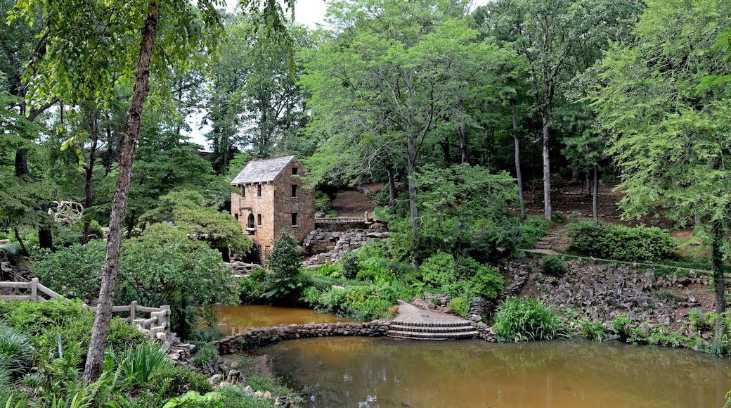 Um edifício rústico de pedra rodeado por vegetação exuberante e um pequeno lago.