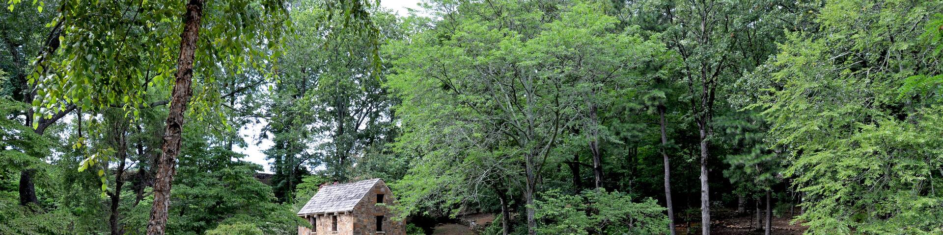 A rustic stone building surrounded by lush greenery and a small pond.