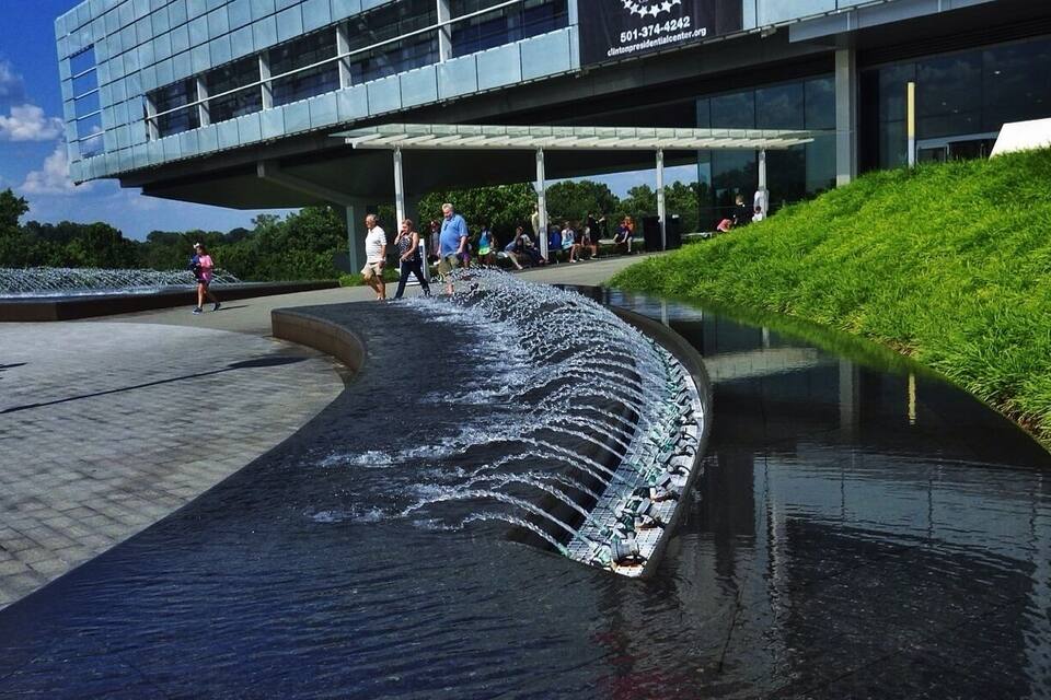 A modern building with a Clinton Presidential Center sign, a water feature, and a grassy area.