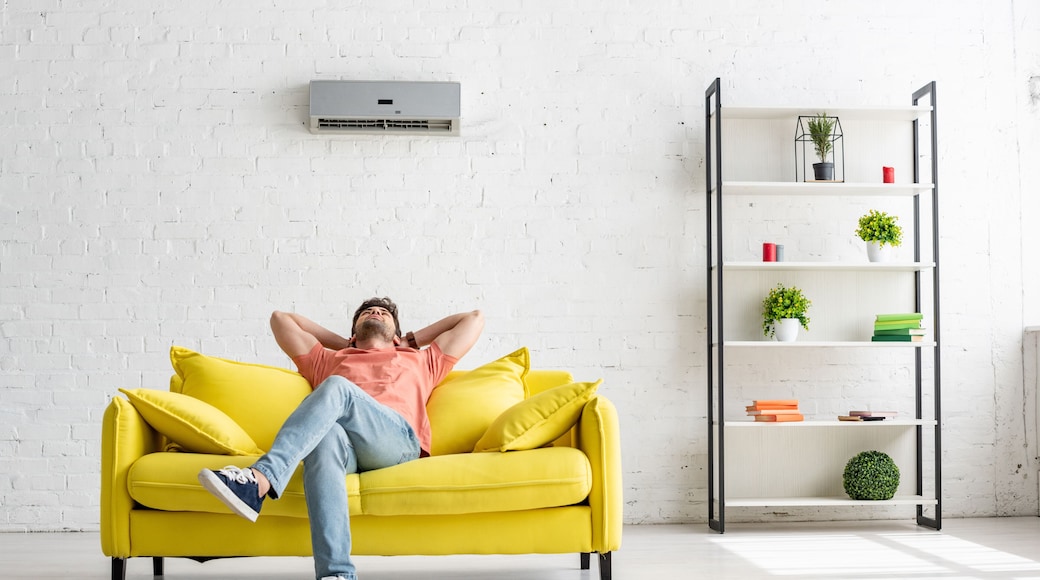 young man sitting on yellow sofa under air conditioner in spacious apartment
