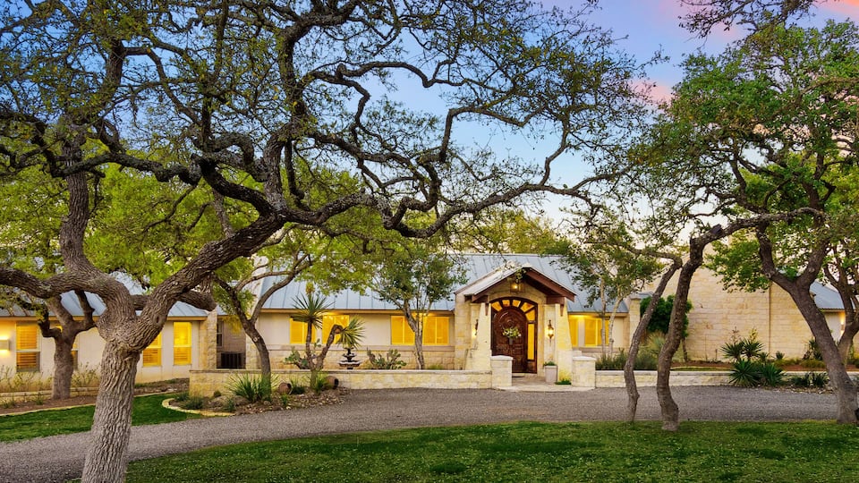 A stone building with a yellow facade and a wooden door, surrounded by trees and a gravel path.