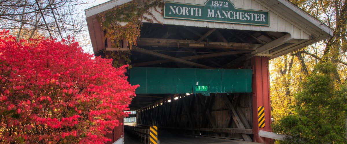 A covered bridge with a sign reading "North Manchester 1872" and a green exit sign.