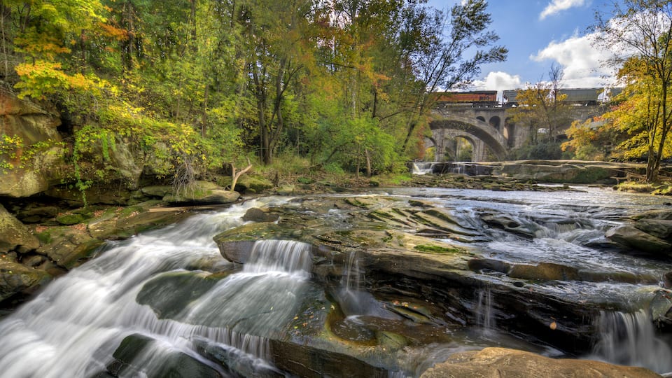 A waterfall, rocky terrain, and a bridge in a forested area.