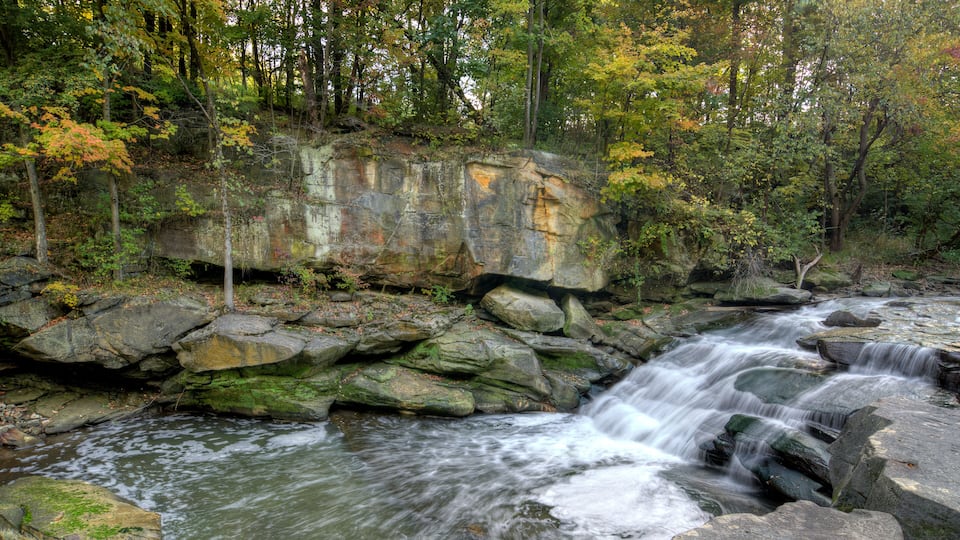 A rocky stream with a waterfall surrounded by autumn foliage.