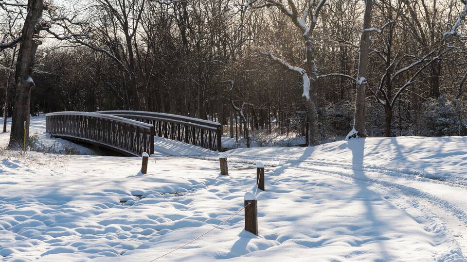 A snow-covered park with a wooden bridge and bare trees.