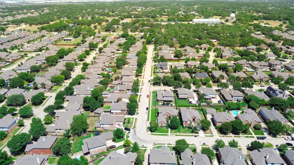 A residential area with houses, streets, and a large building in the distance.