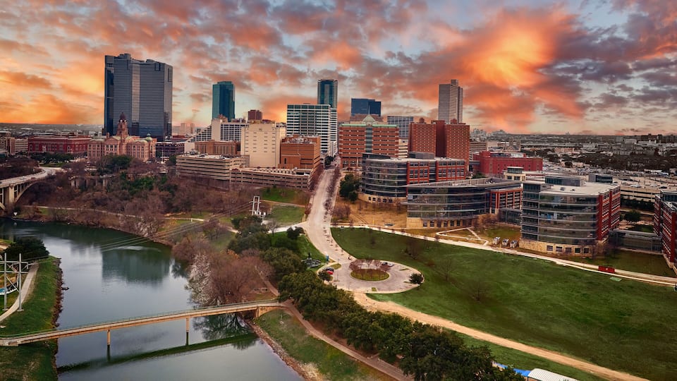 A cityscape with a river, a bridge, and modern buildings under a sunset sky.