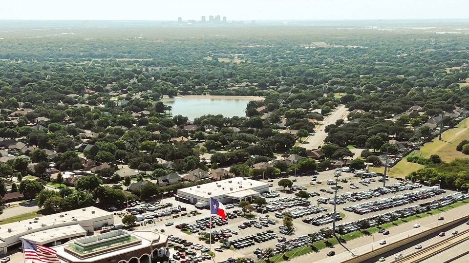 Panorama aerial view NE Loop 820 in North Richland Hills, Texas, showing multilane highway, large retail buildings flat roofs and HVAC units, dealership lots adjacent to green residential zones