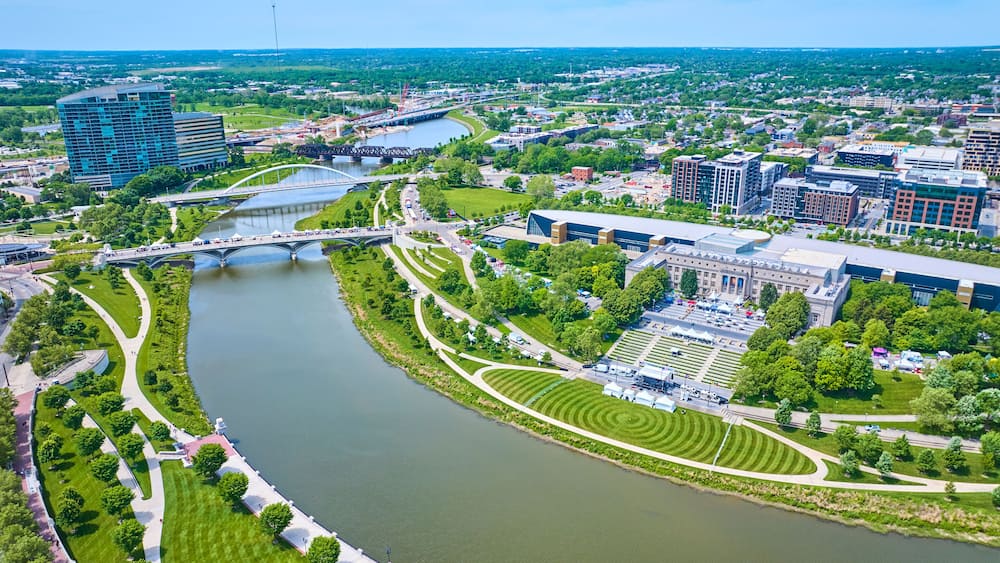 A river winding through a city with modern buildings, a bridge, and well-maintained parks.